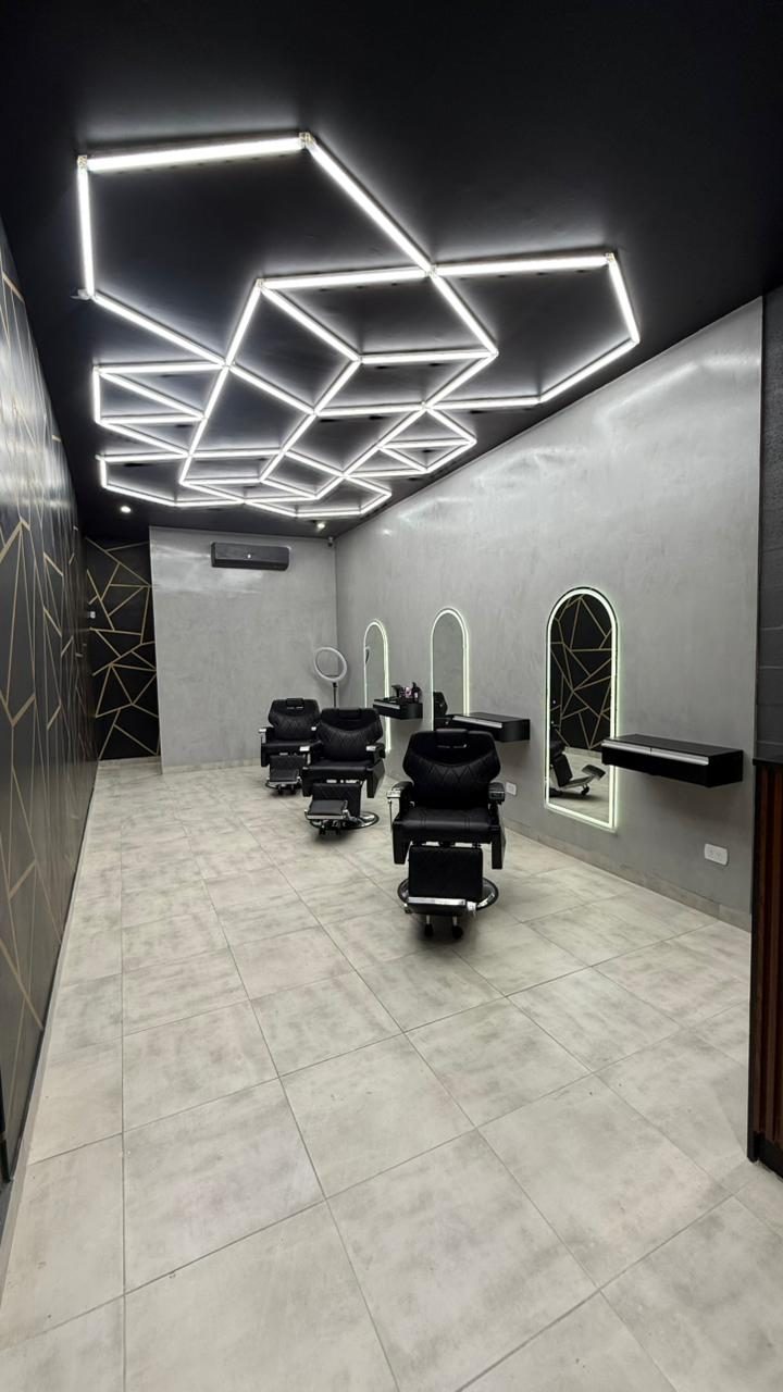 Sala de Royal Barbería sucursal Las Piedras: sillones, espejos arqueados y techo de neón hexagonal